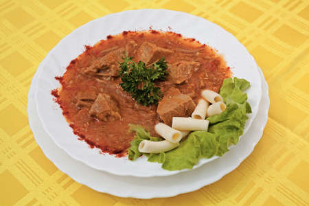 beef goulash with macaroni and lettuce on the plate on the yellow backgroundの写真素材