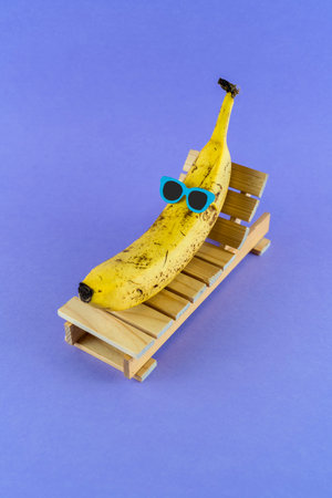 Banana with sunglasses resting on the wooden beach bed. Summer vacation concept on purple backgroundの写真素材