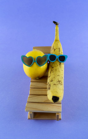 Lemon and banana with sunglasses resting on the wooden beach bed. Summer vacation concept on purple backgroundの写真素材