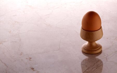 Hard boiled brown egg in wooden cup sitting on stone counterの写真素材