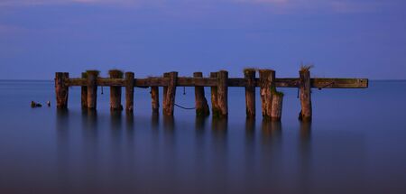 Warm evening light contrasts against a tranquil Lake Ontario as it highlights the remains of an aging pier completely separated from the shore.の写真素材