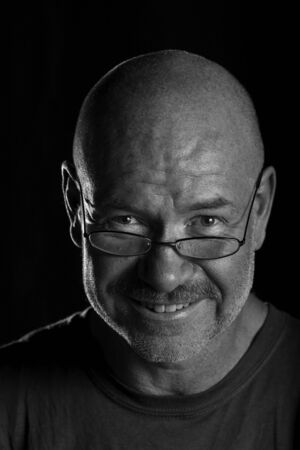 Dramatically lit head shot of older man looking over his glasses and smilingの写真素材