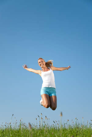 young woman jumping in the air against a blue skyの写真素材