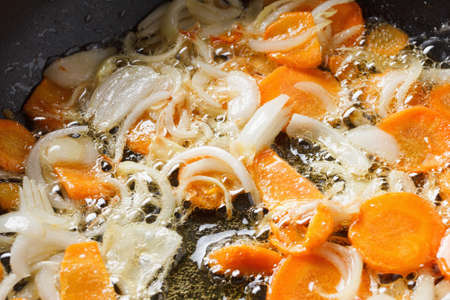Onions and carrots in the pan. Bubbles of sunflower oil in a large frying pan. The cooking processの写真素材