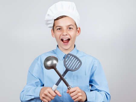 Young cheerful teenager with a ladle and humor in a chef's hat. On white background.の写真素材