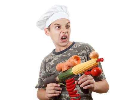 Humorous portrait of a teen boy chef with opened mouth and rifle vegetables, screaming cheers, isolated white backgroundの写真素材