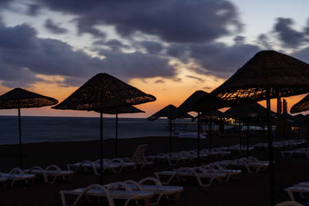 Picturesque sea beach with umbrellas and sunbeds at sunsetの写真素材