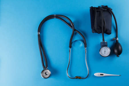 Medical devices stethoscope, tonometer, and thermometer on blue background. Copyspace