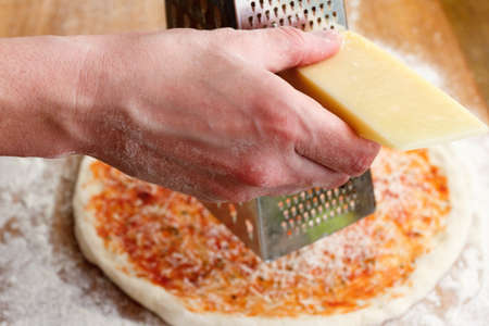 Cook chops grated cheese for pizza covered with sauceの写真素材