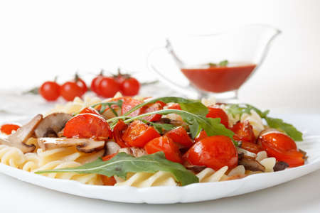 Pasta with mushrooms, cherry tomatoes and tomato sauce. Traditional Italian food. On a white plate closeupの写真素材