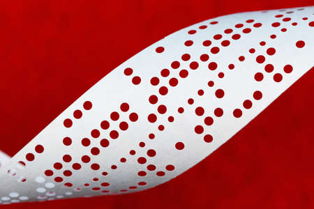 Closeup of perforated punched tape, obsolete data storage, on red backgroundの写真素材