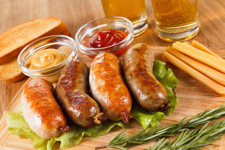 October fest traditional menu, beer and roast beef or chicken sausage  with ketchup, mustard and rosemary. Wooden cutting boardの写真素材