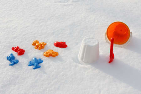 Overhead view on colorful toys, bucket and shovel which are filled up with snow, covered snow,  on the white snowの写真素材