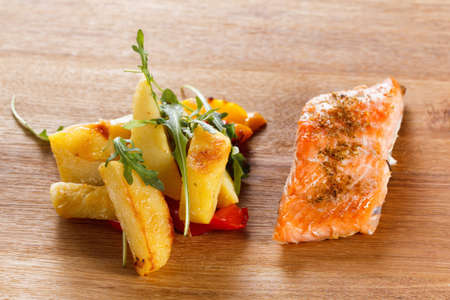 Baked prepared salmon fillet with vegetables, spices and arugula on a plate closeup. Cooking fishの写真素材
