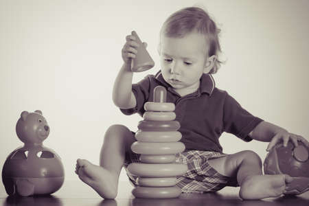 Caucasian baby playing with a toy pyramid. Photo in vintage style of old picturesの写真素材
