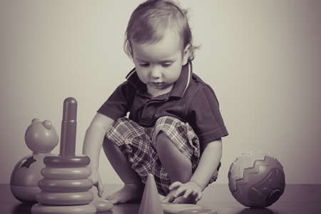 Caucasian baby playing with a toy pyramid. Photo in vintage style of old picturesの写真素材