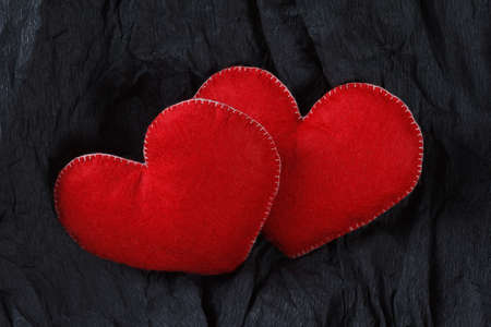 Love concept, red hearts on black paper texture. Dark background with two felt hearts for use in graphic design. Valentine's style, St. Valentine's Day.の写真素材