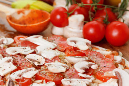 Cooking homemade traditional pizza with salmon, tomatoes,  mushroom and different spices on wooden tableの写真素材
