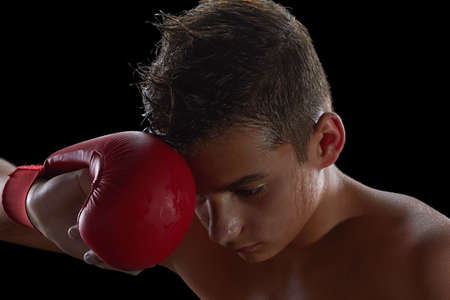 Young boy athlete, boxer or kickboxer gloves after losing or training. Black background.の写真素材