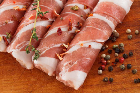 Slices of bacon roll closeup on cutting board with spices, cooking foodの写真素材