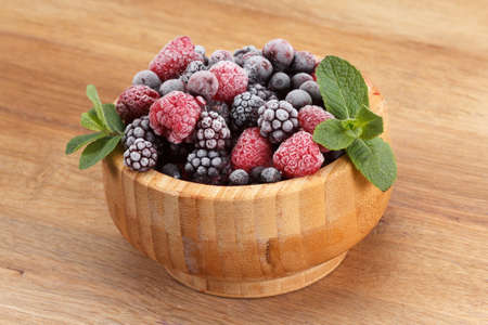 Frozen berries in wooden bowl, covered with ice with mint leaves closeupの写真素材