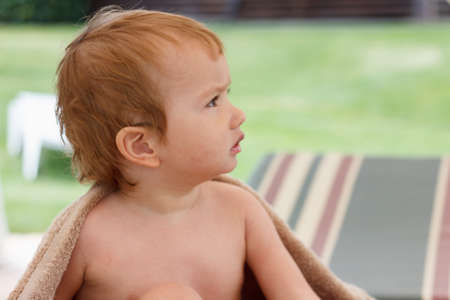Happy boy wrapped in towel sitting on recliner of outdoor swimming poolの写真素材