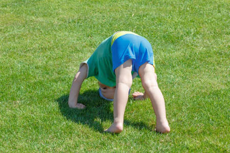 Happy curly barefoot little boy on summer green grass meadow sunny day outdoor, horizontal photo