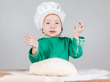 Smiling little cook boy kneading the dough for the cookies, isolated on white background.  Half-length portrait of the table in studioの写真素材