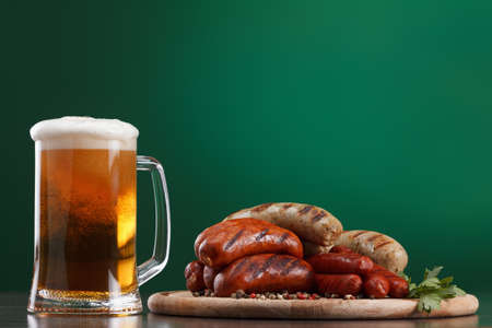 Traditional Oktoberfest menu. Beer being poured into a glass with foam, traditional snacks, sausages grilled. Copyspace with green backgroundの写真素材