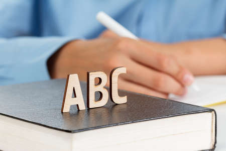 Boy writes in a school notebook, wooden letters ABC on the book. Back to school conceptの写真素材