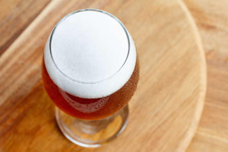 A glass of cold foamy beer on wooden background. Mug closeup with copyspace. Overhead view.