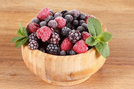 Frozen berries in wooden bowl, covered with ice with mint leaves closeupの写真素材