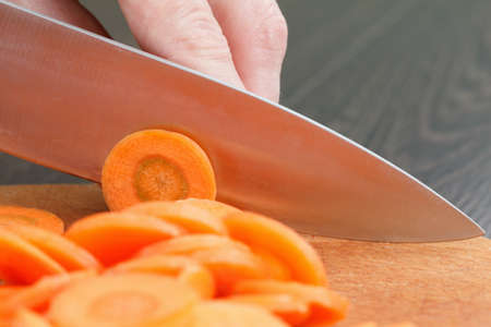 Chefs hands chopping carrot on wooden cutting board