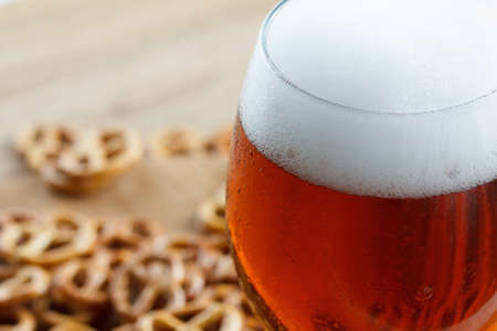 A glass of cold foamy beer with pretzels. Bavarian Oktoberfest snacks and drink on wooden background