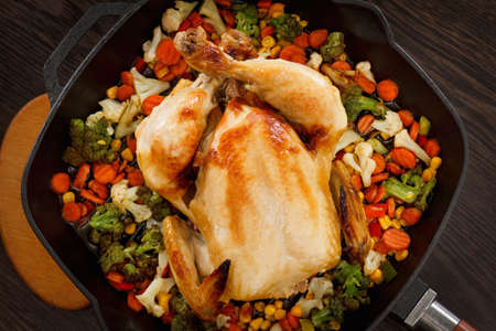 Roasted chicken and vegetables in pan on the wooden tableの写真素材