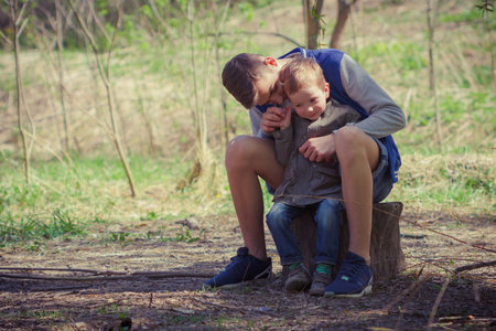 Two cute kids sitting together on log in forest. Elder and younger brothersの写真素材