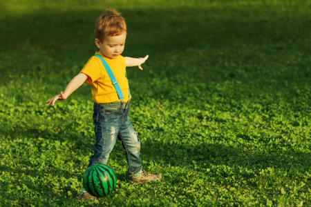 Cute positive kid, playing happily with ball on green meadow. A happy childhoodの写真素材