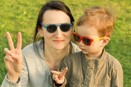 The son kisses and hugs his mom in sunglasses outdoors. Mother and her child having fun together. Little kid express the love to his mommy.の写真素材