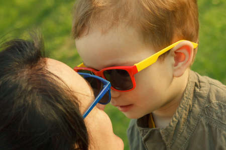 The son kisses and hugs his mom in sunglasses outdoors. Mother and her child having fun together. Little kid express the love to his mommy.の写真素材