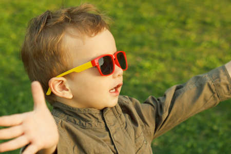 Cute red-haired boy in sunglasses highlighted with a sunset sun rays, reaches out to the sunset. A happy childhood.の写真素材