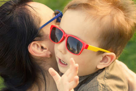 The son kisses and hugs his mom in sunglasses outdoors. Mother and her child having fun together. Little kid express the love to his mommy.の写真素材