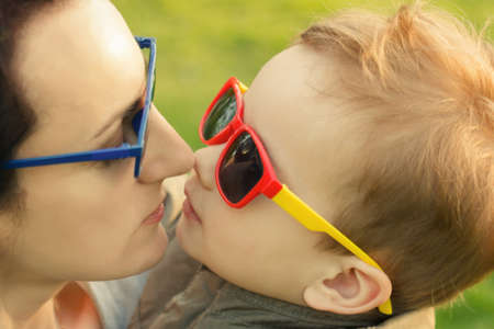 The son kisses and hugs his mom in sunglasses outdoors. Mother and her child having fun together. Little kid express the love to his mommy.の写真素材