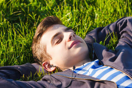 Young man listening music from smart phone on the grass in the park.の写真素材