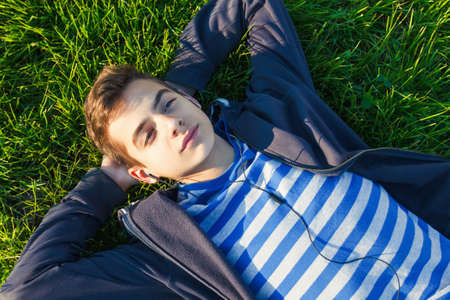 Young man listening music from smart phone on the grass in the park.の写真素材