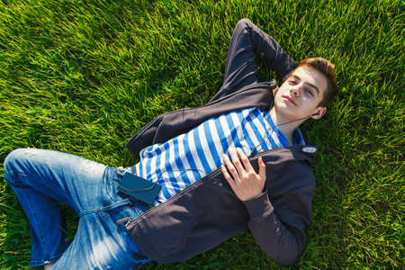 Young man listening music from smart phone on the grass in the park.の写真素材