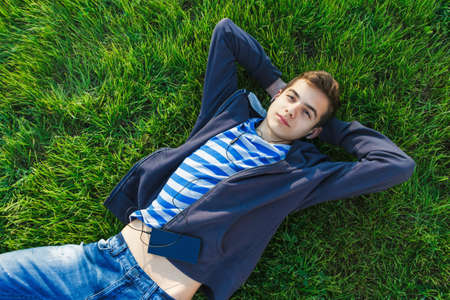 Young man listening music from smart phone on the grass in the park.の写真素材