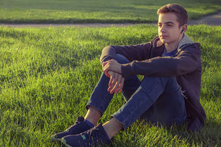Young man listening music from smart phone on the grass in the park.の写真素材