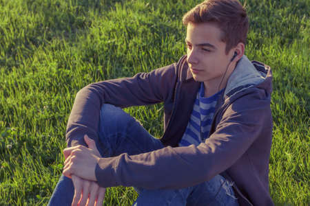 Young man listening music from smart phone on the grass in the park.の写真素材