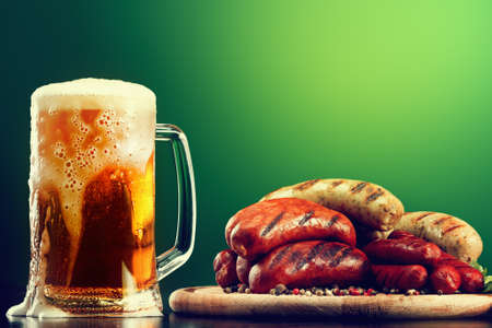 Mug of beer with grilled sausages on green background. Oktoberfest traditional drink and food in pubの写真素材