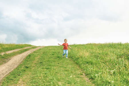 Little boy running across the field on the lawn on a hot summer dayの写真素材